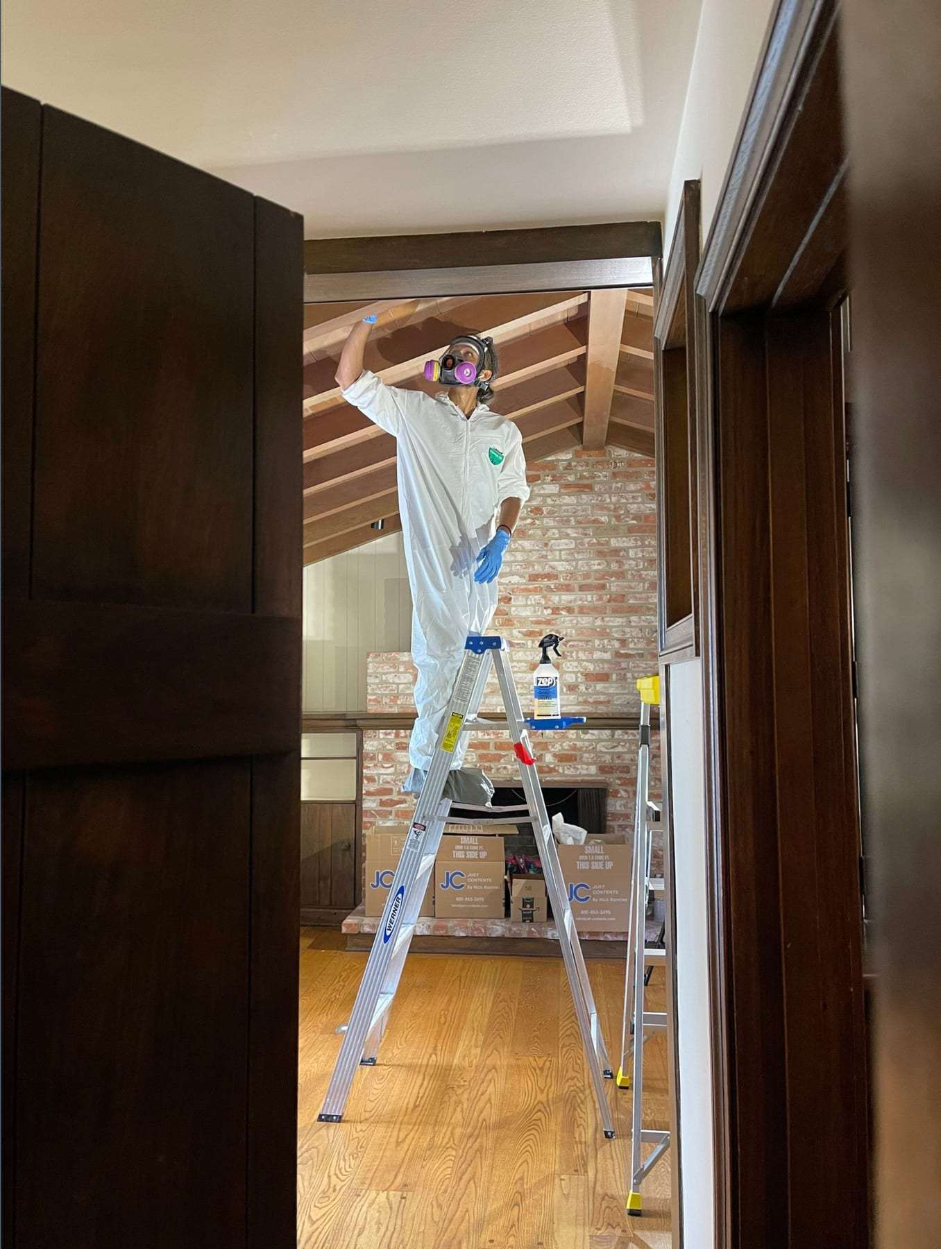 Technician in a protective suit cleaning a ceiling from a ladder