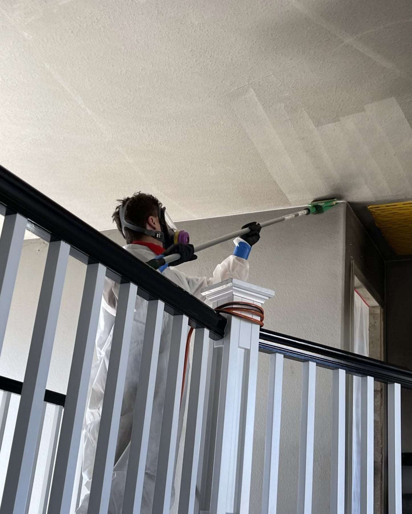 Technician in a respirator cleaning a high ceiling over a stair railing