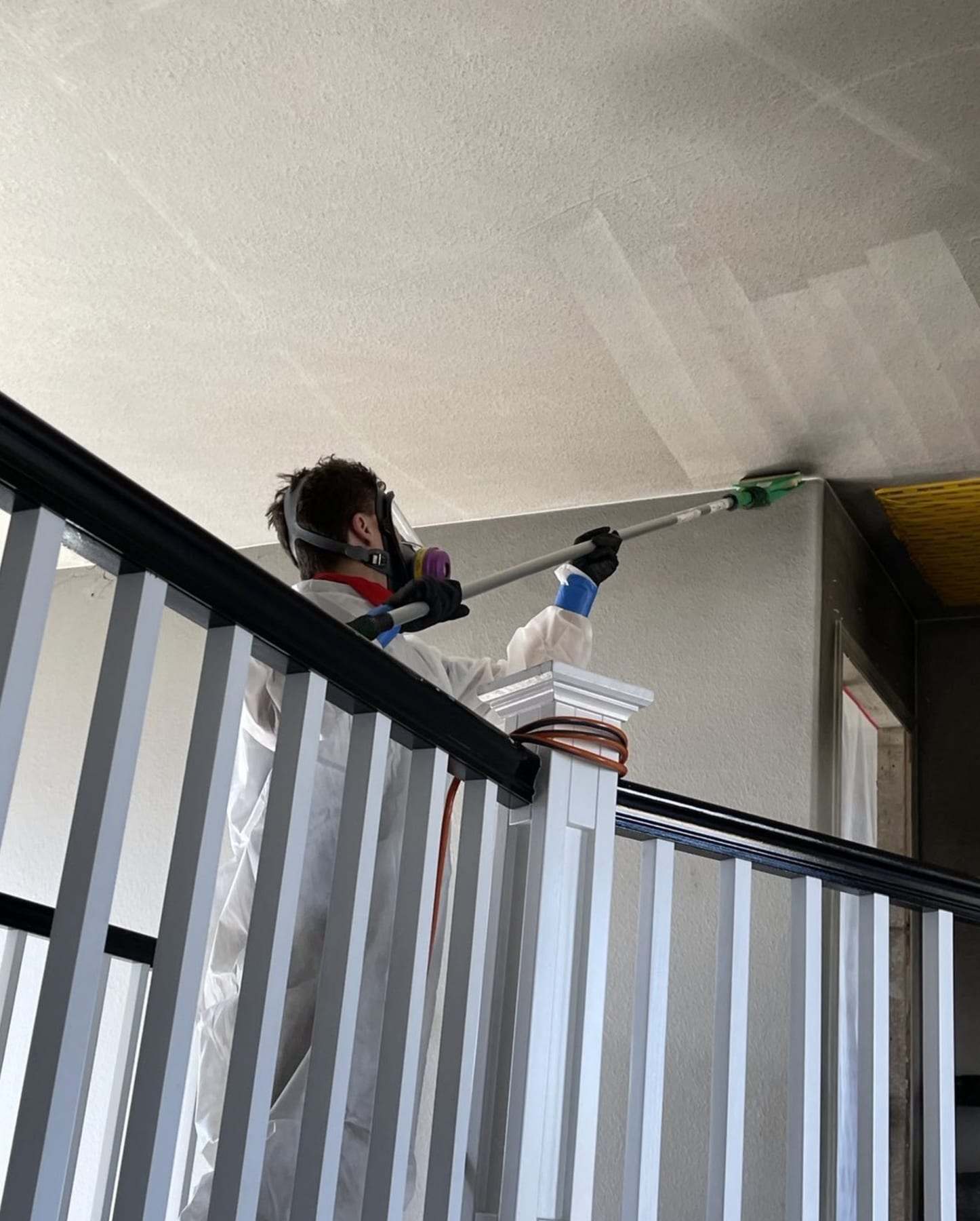 Technician in a respirator cleaning a high ceiling over a stair railing